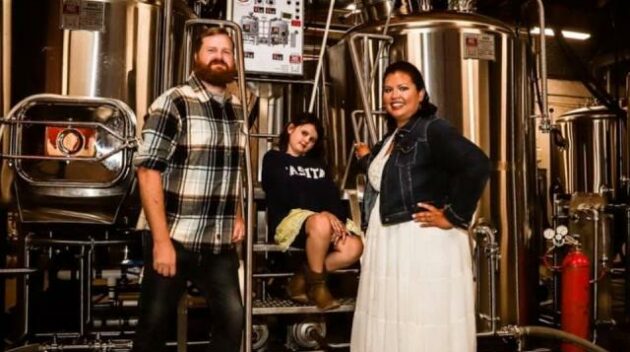 New owners of Casita Brewing pose with their child in front of fermenter - Discover Wilson