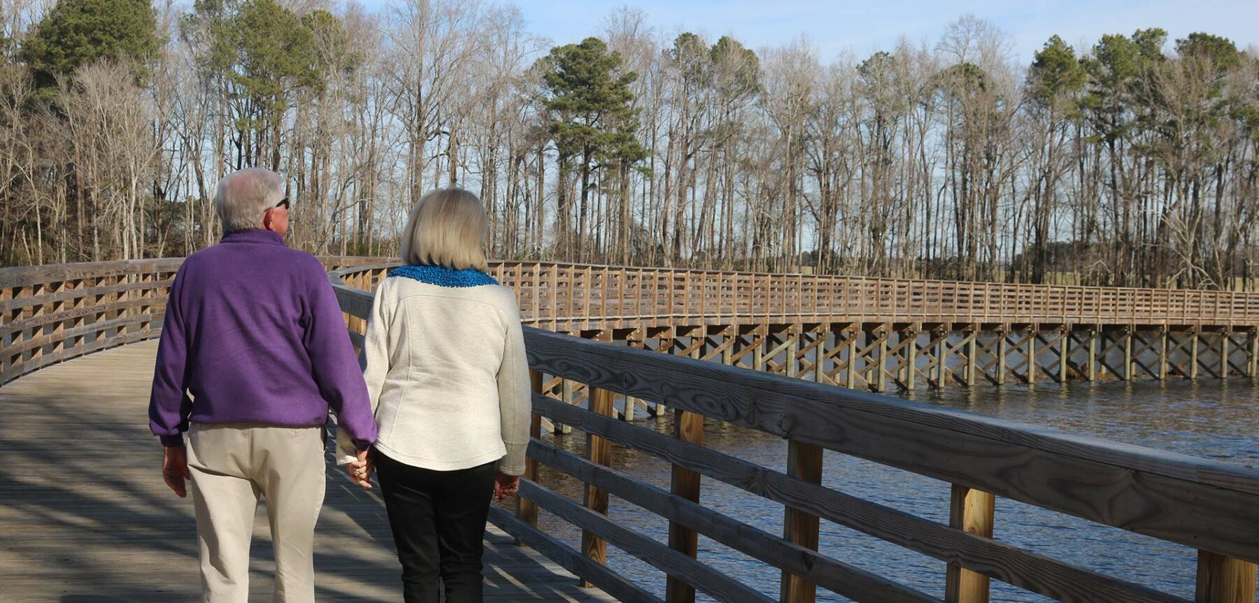 Retirees holding hands and walking across wooden bridge in Wilson, NC - Discover Wilson